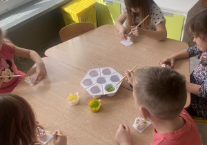 Dzieci przy stoliku malują farbami baranki wykonane z masy solnej