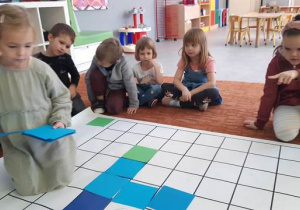 Dziewczynka układa niebieskie kwadraty na macie do kodowania.