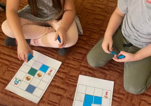 Dzieci układają niebieskie kwadraty na kratownicy.