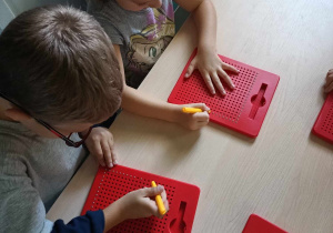 Dzieci ćwiczą koordynację wzrokowo-ruchową tworząc obrazki na tabliczkach z magnetycznymi kulkami