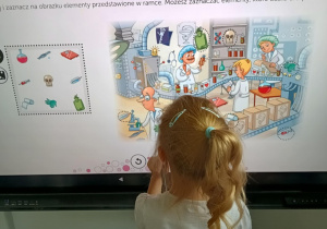 Dziewczynka rozwiązuje na ekranie multimedialnym zadanie doskonalące analizę wzrokową