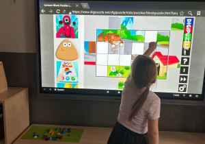 Dziewczynka układająca puzzle na tablicy multimedialnej